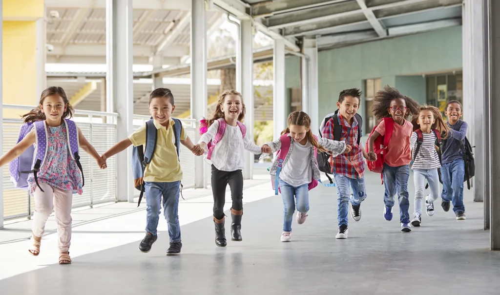 Group of children with backpacks running together in a school corridor