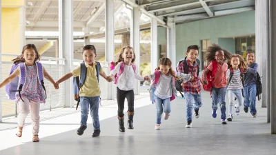 Group of children with backpacks running together in a school corridor